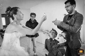 Playful Wedding Prep Moment at Bride's Home, Saint-Paul-Sur-Save, Haute-Garonne This wedding photo captures a playful moment with the bride, her brother presenting a different lipstick option, and the children sharing their opinions, taken at the future couple's home in Saint-Paul-Sur-Save, Haute-Garonne.